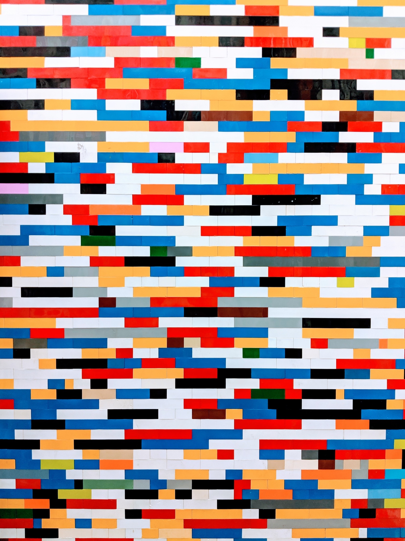 Photograph of a wall built from many small multicoloured rectangular tiles arranged in a brick-like pattern